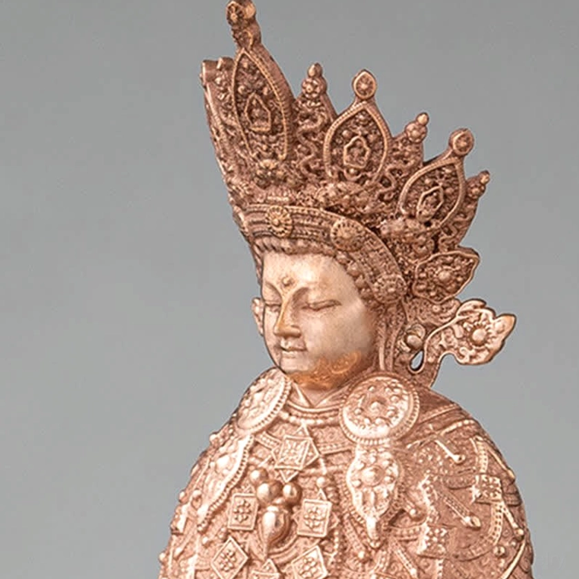 Close-up detail of Shakyamuni Buddha statue showing serene facial features, ornate crown, and intricate chest carvings on pure copper