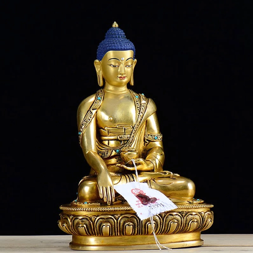 Shakyamuni Buddha copper statue left three-quarter angle showing detailed robe and gilt bronze craftsmanship with black studio backdrop
