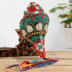 Handcrafted shankha conch shell decoration with turquoise and copper Buddha inlays, displayed on wooden table with braided tassel