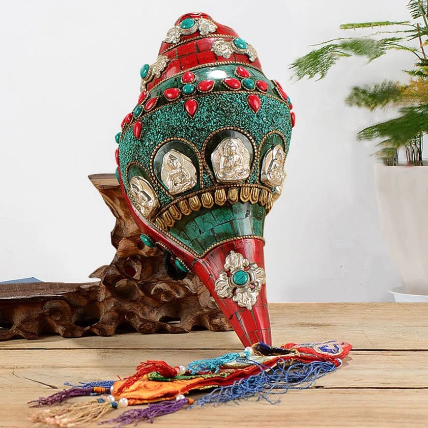 Handcrafted shankha conch shell decoration with turquoise and copper Buddha inlays, displayed on wooden table with braided tassel