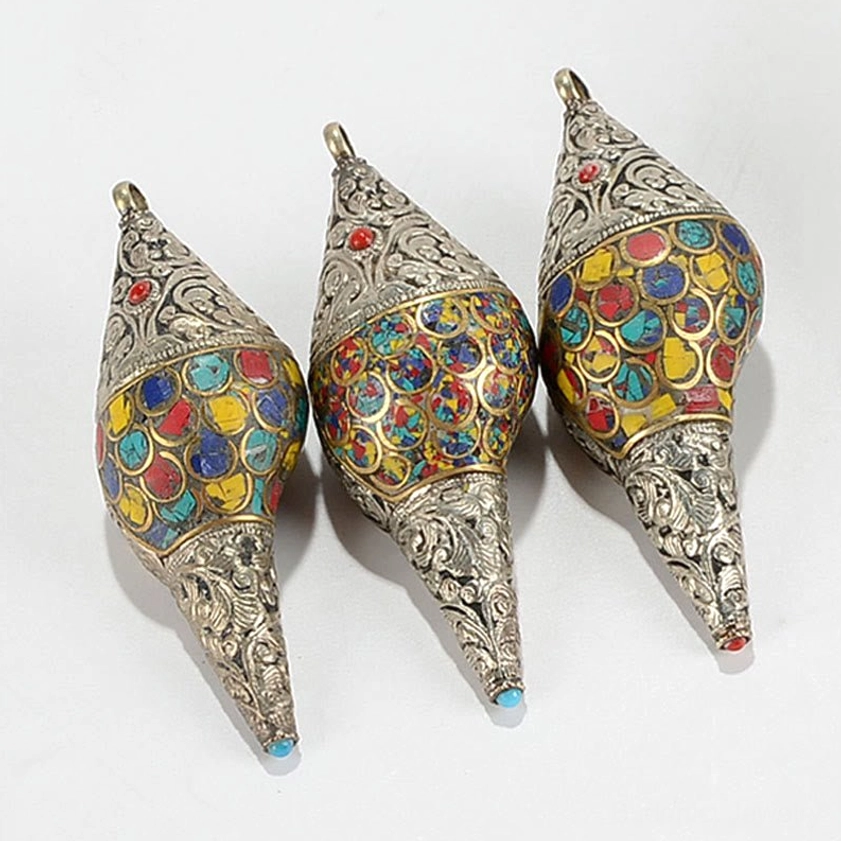 Extreme close-up of sacred conch shell front tip showing carved silver metalwork and red gemstone accent with hanging loop