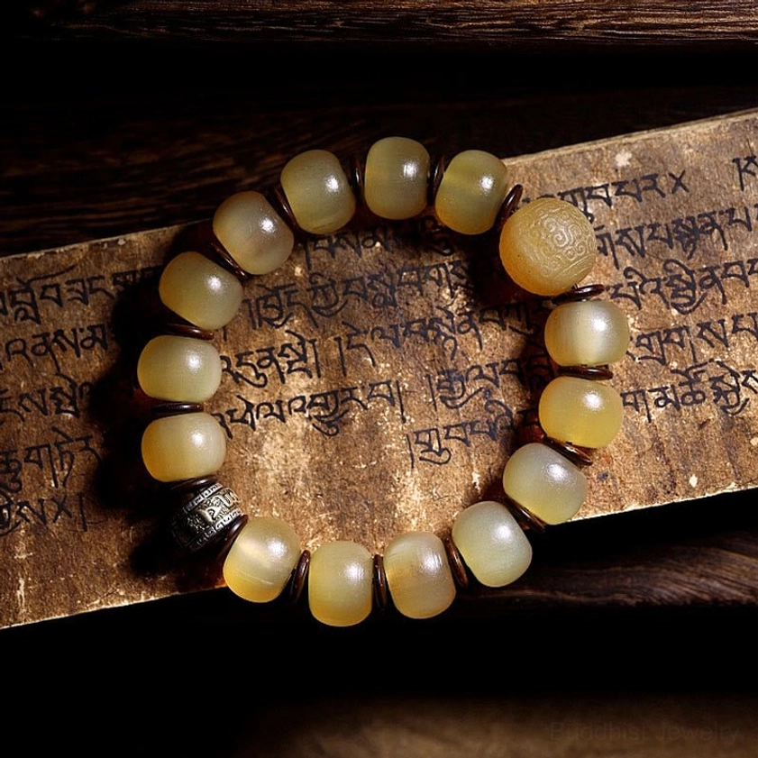 Om Mani Padme Hum sheep horn bracelet featuring barrel-shaped beads with single metal spacer bead on Tibetan Buddhist scripture background