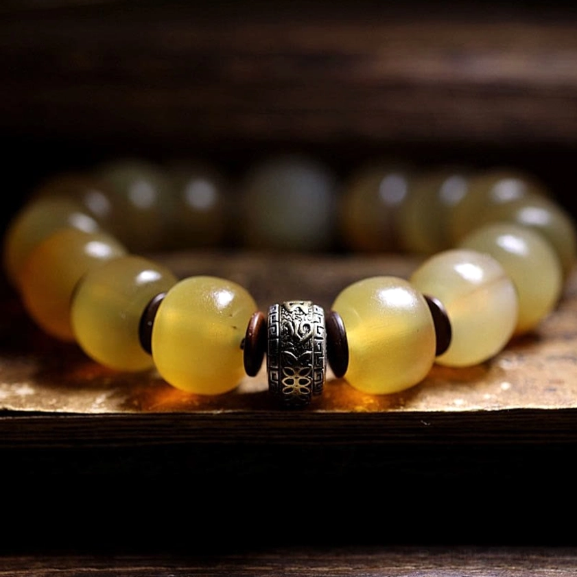 Side close-up of sheep horn Om Mani bracelet featuring carved Tibetan silver spacer with glossy translucent beads on wooden surface