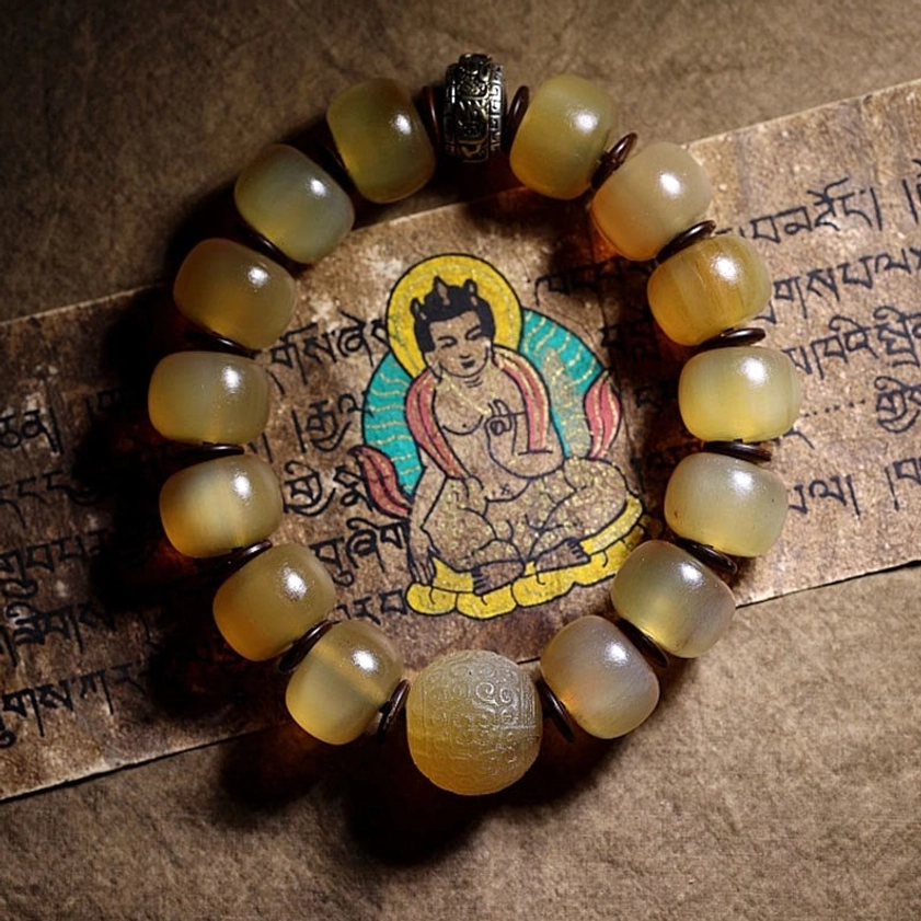 Complete Om Mani Padme Hum sheep horn bracelet with decorative metal spacer displayed on sacred Tibetan Buddhist scripture in top-down view