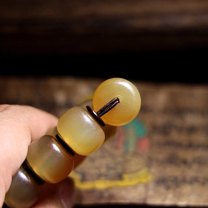 Macro close-up of handmade sheep horn Om Mani bracelet featuring glossy barrel beads and dark spacer rings on Thangka religious art background