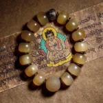 Natural sheep horn Om Mani Padme Hum bracelet with Tibetan silver spacer displayed on sacred Buddhist scripture, warm translucent yellow beads in flat lay photography