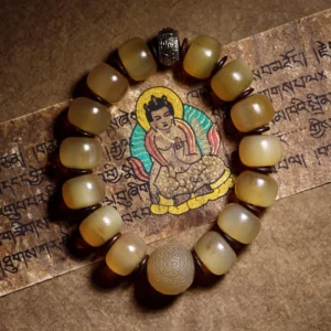 Natural sheep horn Om Mani Padme Hum bracelet with Tibetan silver spacer displayed on sacred Buddhist scripture, warm translucent yellow beads in flat lay photography