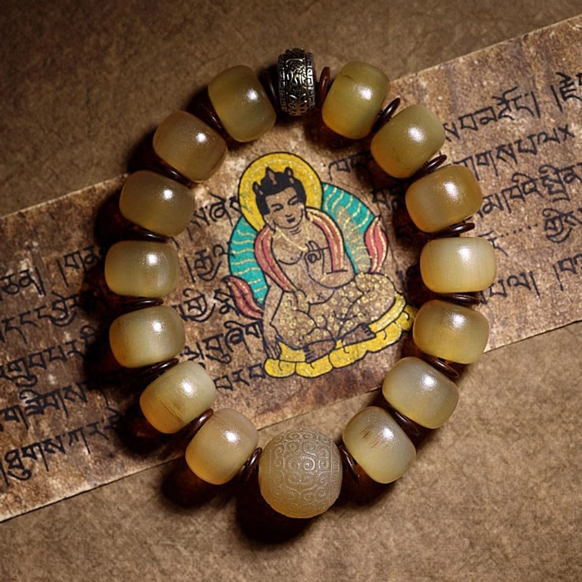 Natural sheep horn Om Mani Padme Hum bracelet with Tibetan silver spacer displayed on sacred Buddhist scripture, warm translucent yellow beads in flat lay photography