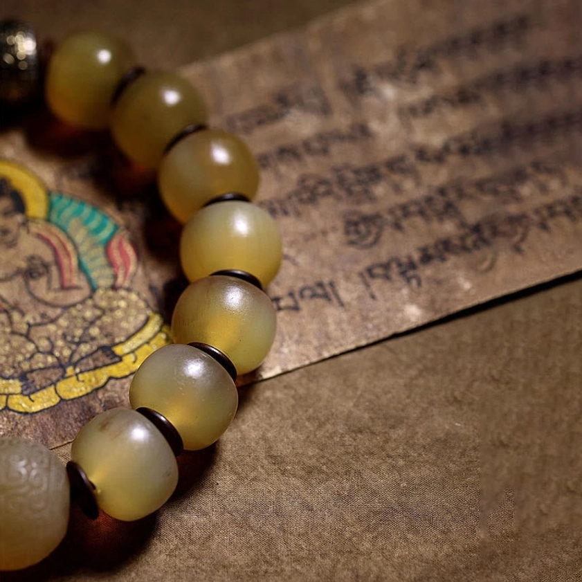 Partial view of natural sheep horn Buddhist bracelet showing translucent yellow beads laid on Buddha print meditation scripture paper