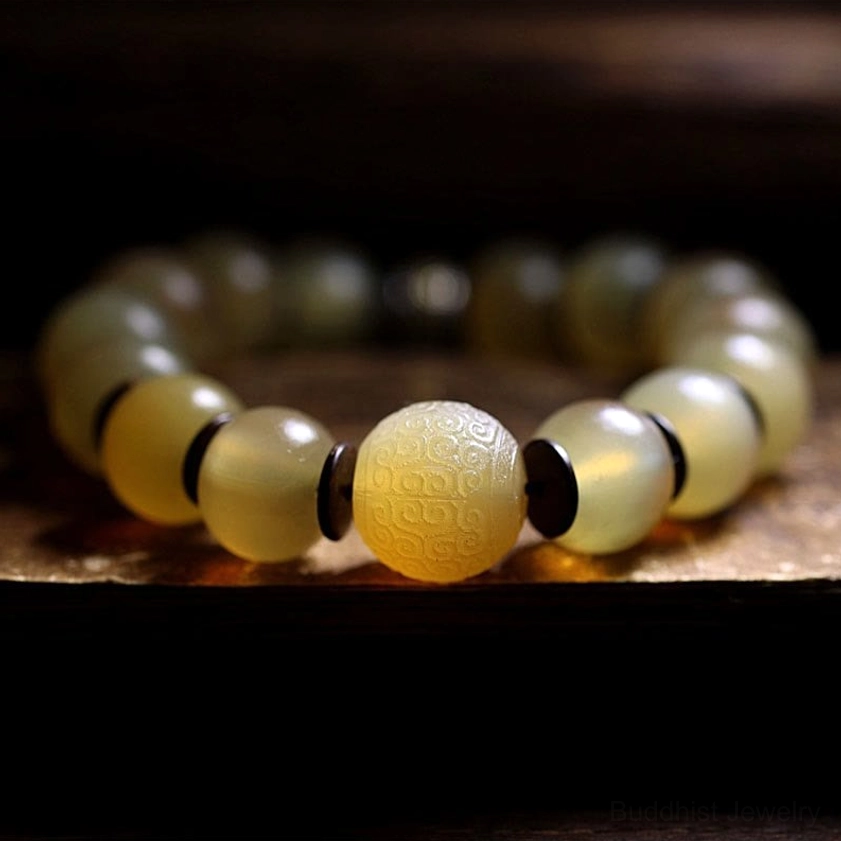 Natural sheep horn Buddhist bracelet showing uniform translucent finish and patterned metal central bead on dark wooden background