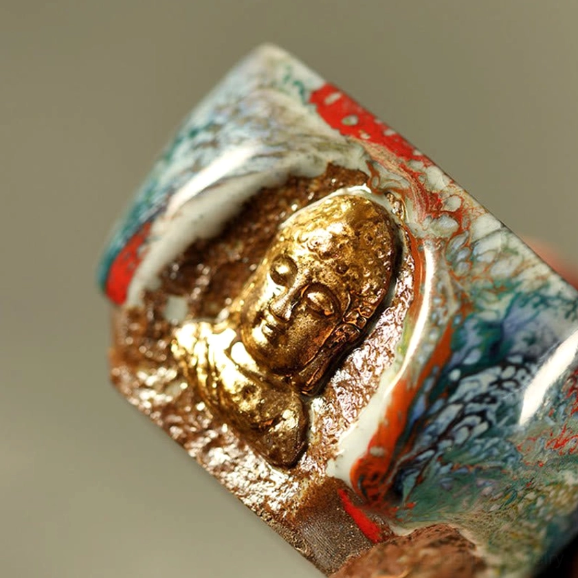Close-up front side view of square Shino ceramic teacup with detailed gilded Buddha sculpture, rough clay base, and flowing blue-red glaze pattern
