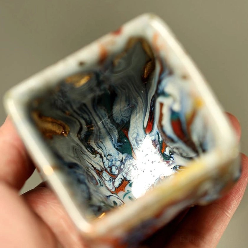 Square ceramic Buddha teacup interior top-down view held by hand showing smooth marbled glaze interior with subtle gilded Buddha accents inside