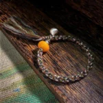 Handmade 990 sterling silver amber steelyard weight bracelet with protective charm on wooden surface and woven fabric