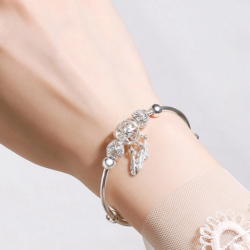 Side oblique wear view of silver dream catcher buddhist protection bracelet on female wrist showing slim metal band and single feather tassel