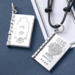 Sterling silver Buddhist sutra book pendant necklace with lotus engraving and hinged flip design, oblique top view on dark blue background