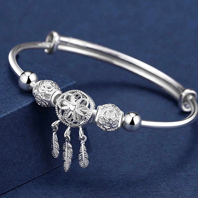Handcrafted silver dream catcher buddhist blessing bracelet with hollow carved beads and feather tassel pendants, displayed in oblique top-down view