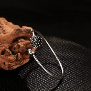 Silver lotus open cuff bangle with detailed bloom and bud charm, left side view on natural driftwood background