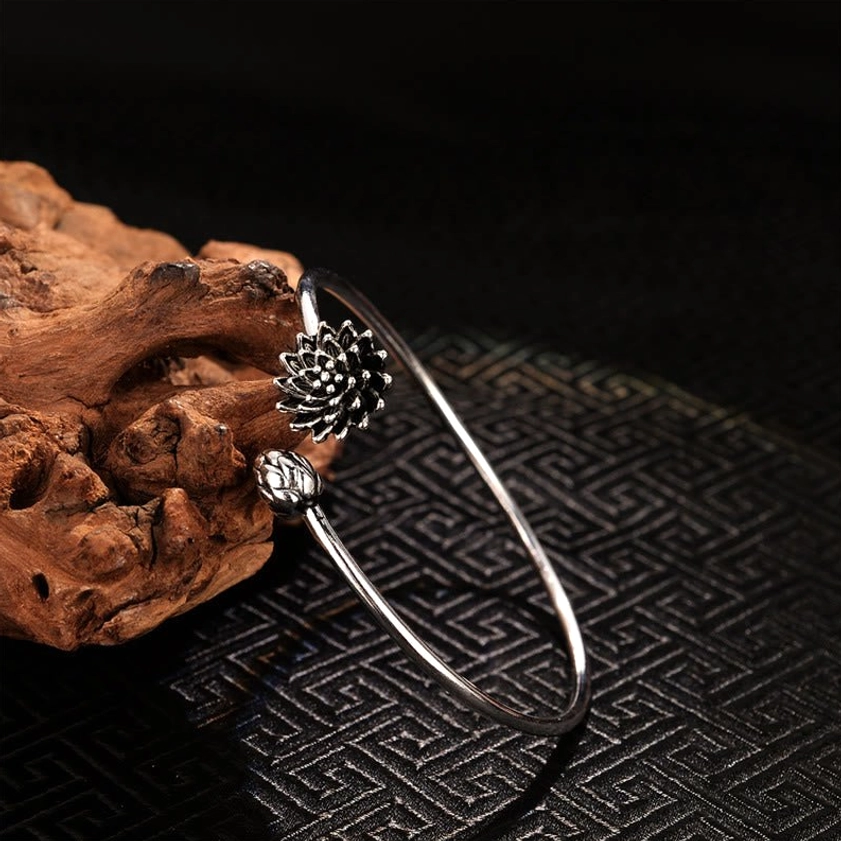 Silver lotus open cuff bangle with detailed bloom and bud charm, left side view on natural driftwood background