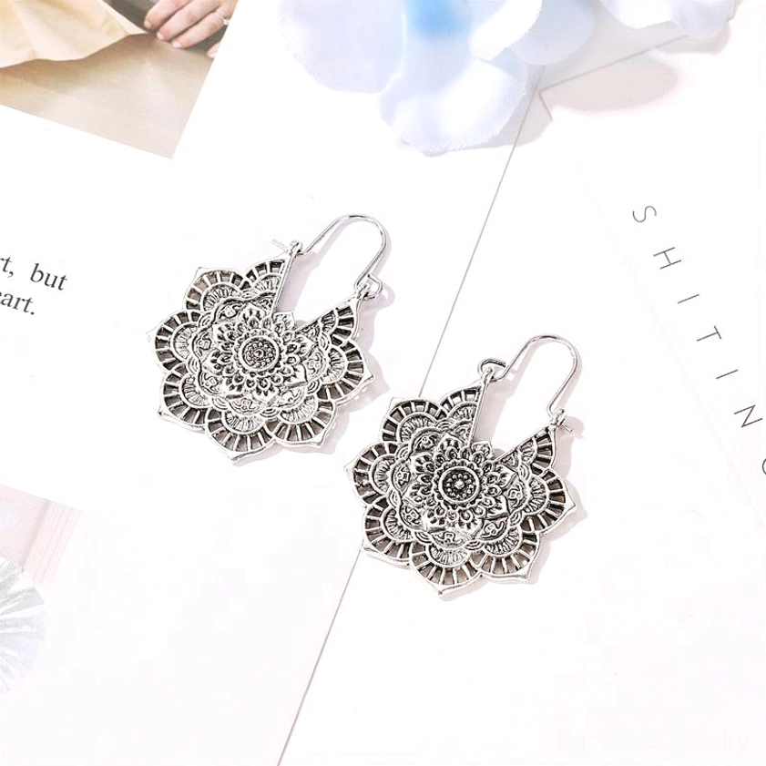 Antique silver lotus drop earrings with filigree floral motif and hoop earwire closure on printed background