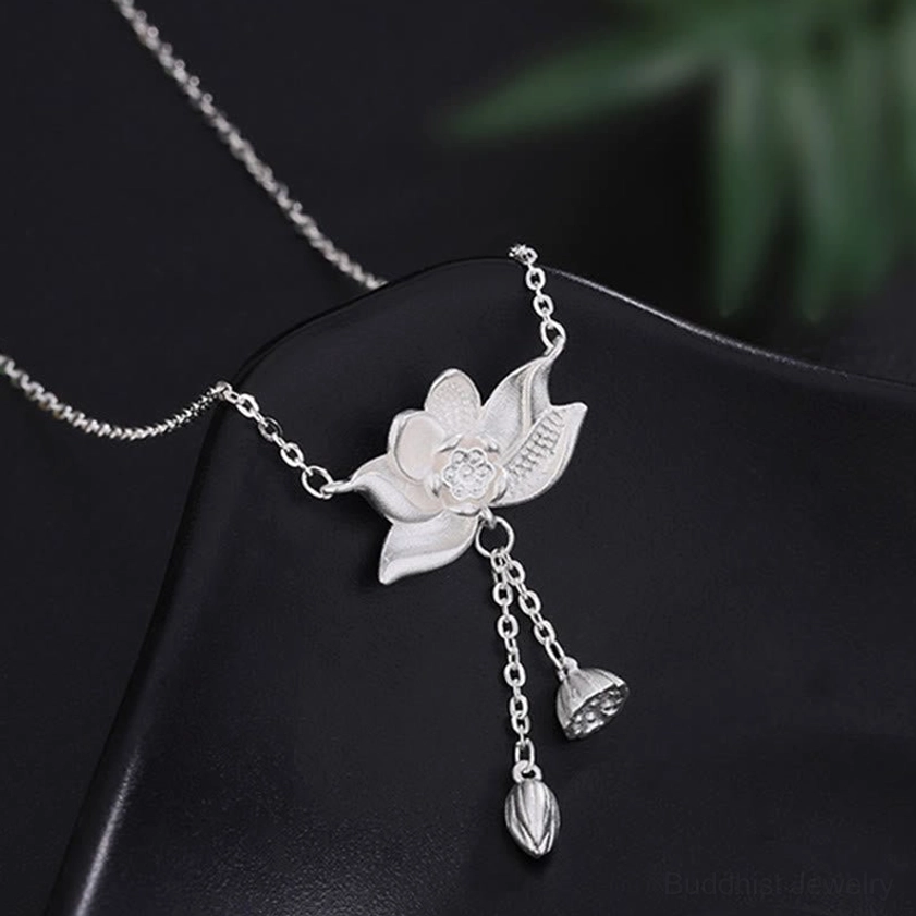 Close-up front view of 999 sterling silver lotus pendant with intricate carving detail, featuring pod and bud charms on black leather pad