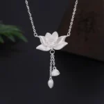 999 sterling silver lotus flower pendant necklace with carved pod and bud tassel, displayed on dark studio background with green foliage accent