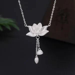 999 sterling silver lotus flower pendant necklace with carved pod and bud tassel, displayed on dark studio background with green foliage accent