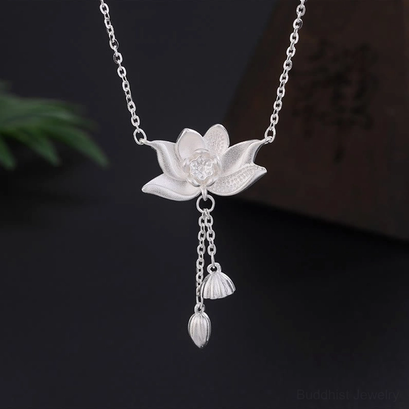999 sterling silver lotus flower pendant necklace with carved pod and bud tassel, displayed on dark studio background with green foliage accent