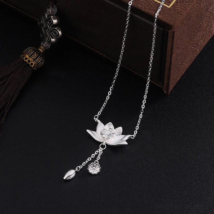 Sterling silver lotus necklace with mixed drop pendants shown from side angle on vintage wooden box background