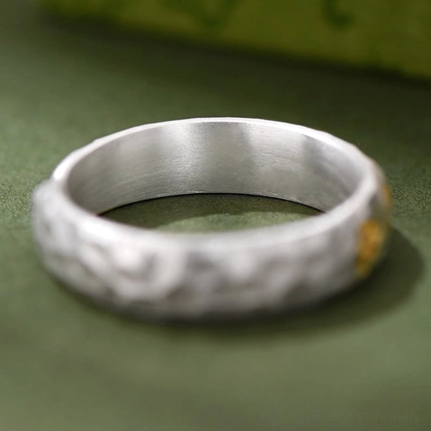Hammered silver band ring with partial gold decoration, flat lay top-down view showing mantra detail