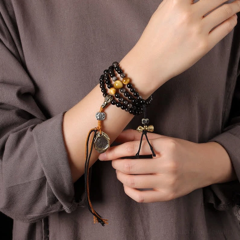 Silver Sheen Obsidian Buddhist protection necklace worn on wrist showing metal charms and brown tassel