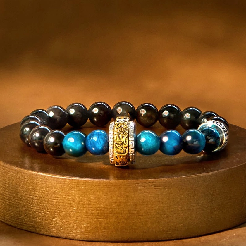 Silver Sheen Obsidian Blue Tiger Eye Buddhist protection bracelet with Om Mani Padme Hum charm, flat lay overhead view on warm wooden surface