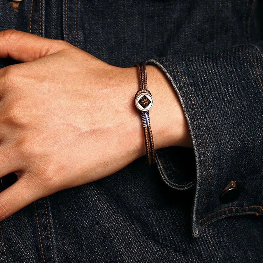 Woven silver Buddhist string bracelet on right wrist displaying decorative metal buckle detail against denim background