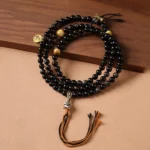 Silver Sheen Obsidian Garuda Buddhist protection necklace with black mala beads and golden metal accents on wooden surface