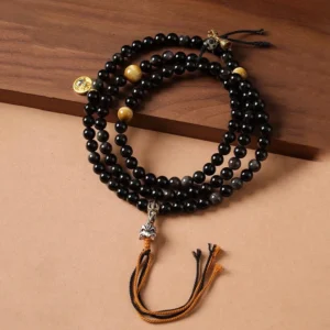 Silver Sheen Obsidian Garuda Buddhist protection necklace with black mala beads and golden metal accents on wooden surface