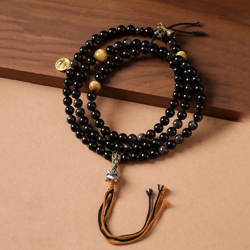 Silver Sheen Obsidian Garuda Buddhist protection necklace with black mala beads and golden metal accents on wooden surface