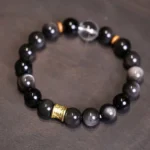 Silver Sheen Obsidian Om Mani Padme Hum Buddhist bracelet with white crystal and gold accents on dark background