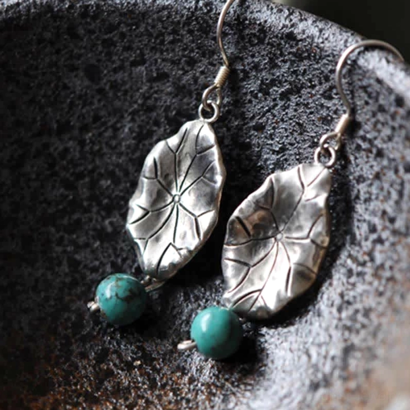 Close-up of 925 sterling silver lotus leaf earrings with turquoise stones on ceramic