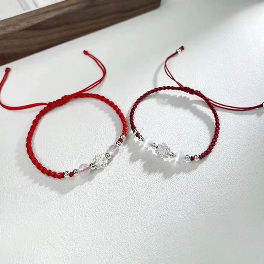 Simple Buddhist string protection bracelet with silver decorative beads and red-black thin cords on tabletop