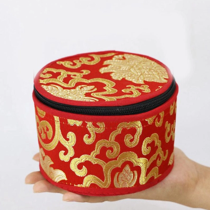 Red singing bowl storage pouch with gold floral embroidery held in palm, overhead view