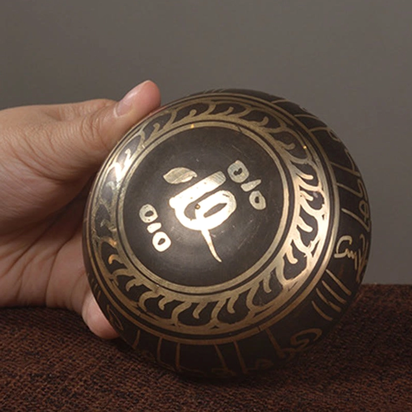 Bottom view of Buddhist singing bowl showing gold flame border and sacred symbols engraved on bronze surface