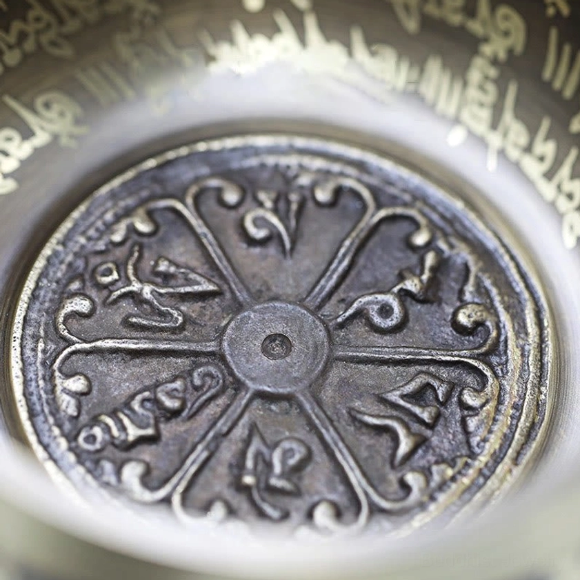 Macro close-up of aged bronze singing bowl bottom showing detailed Vajra and sacred mantra engravings
