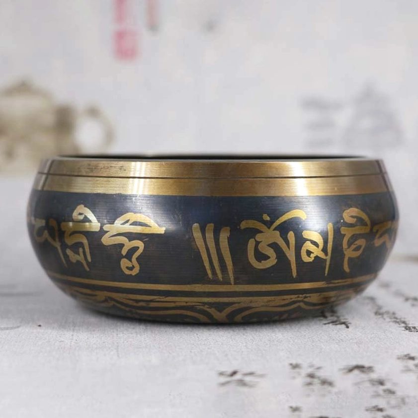 Black brass Buddhist meditation singing bowl with golden Sanskrit Om Mani Padme Hum inscriptions, displaying polished gold trim in eye-level view