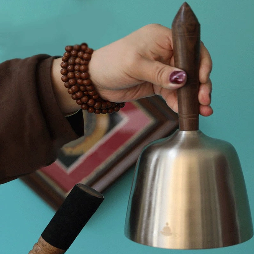 Hand holding Buddhist singing bowl with prayer beads and wooden mallet, spiritual meditation setup