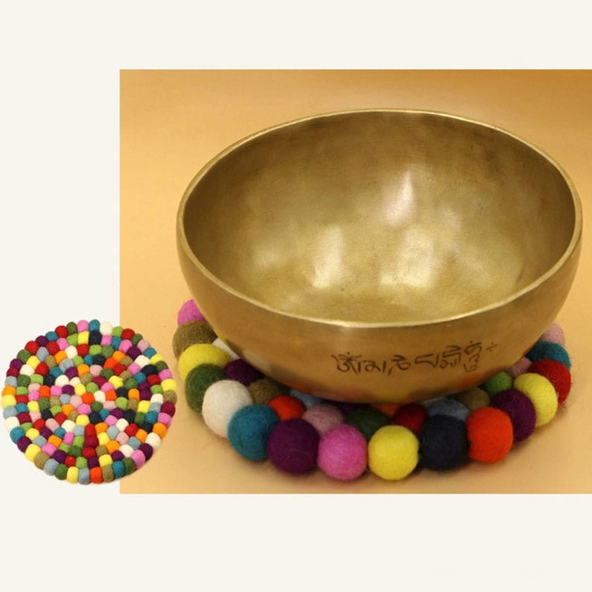 Engraved Buddhist singing bowl resting on handmade felted wool cushion on wooden shelf