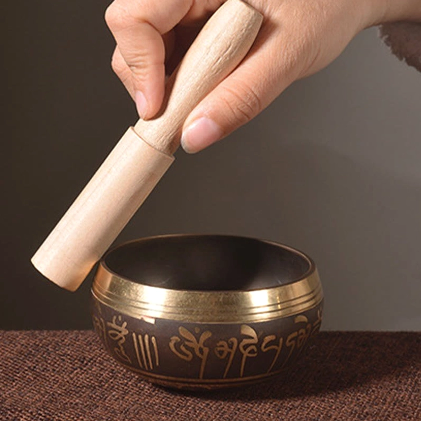 Wooden mallet striking the side of black bronze Buddhist singing bowl on tabletop for meditation practice