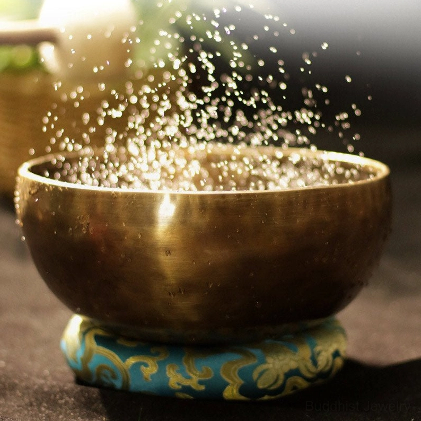 Buddhist singing bowl with water droplets on blue floral cushion demonstrating sound healing resonance