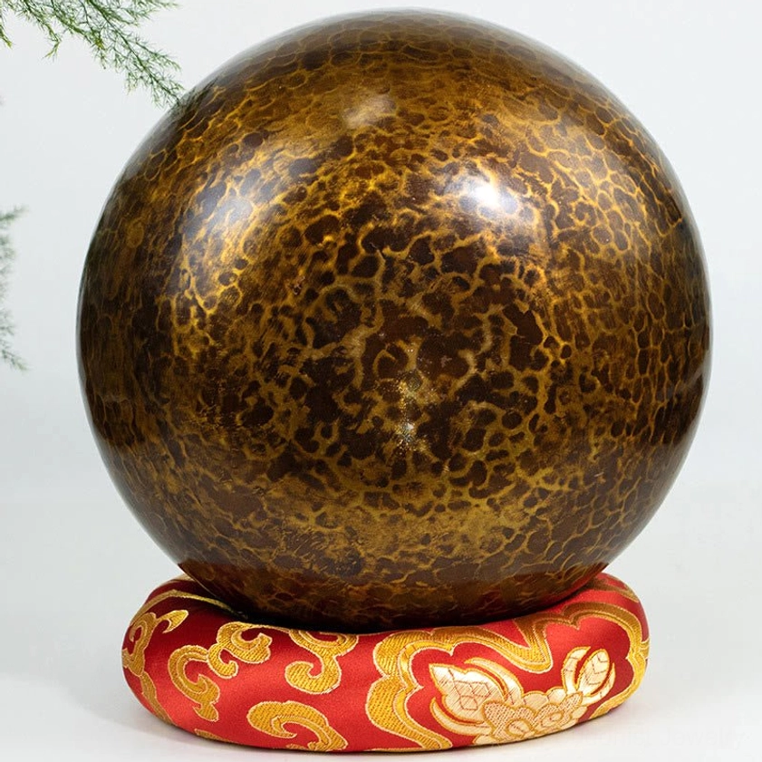 Buddhist singing bowl side view on embroidered cushion displaying full spherical shape and hammer-crackle texture