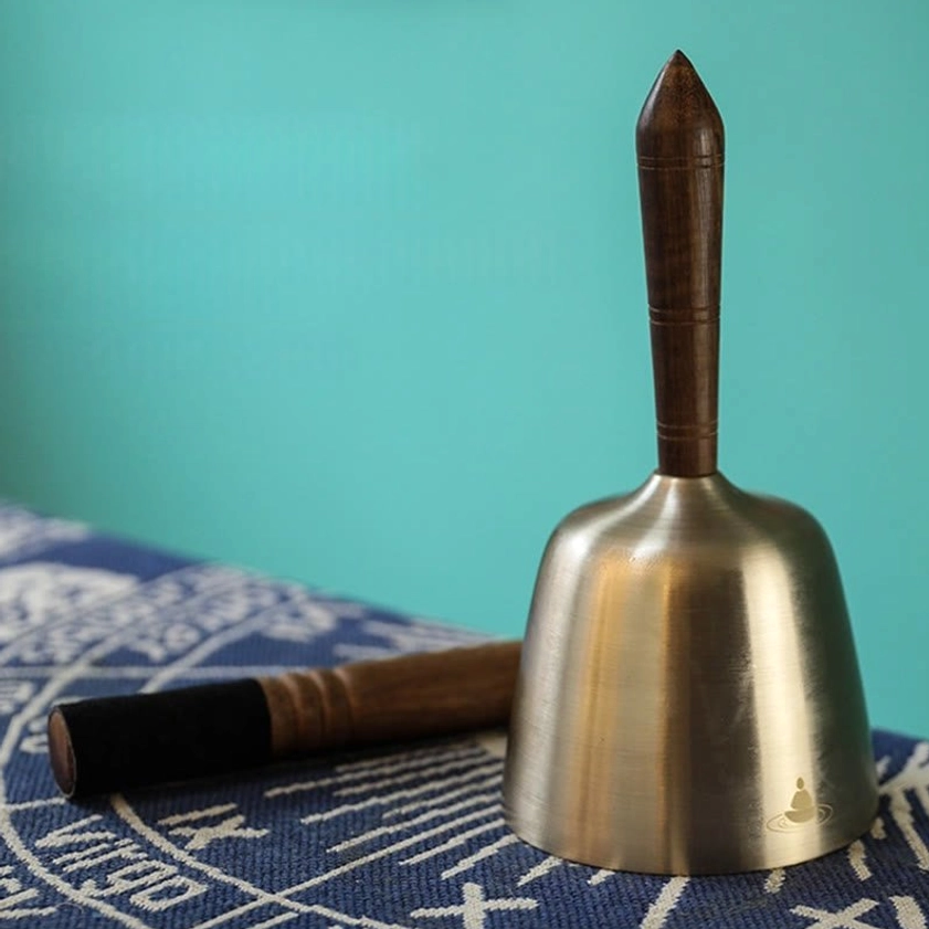 Standing singing bowl on table with wooden mallet beside showing brushed metal finish and dark wooden handle
