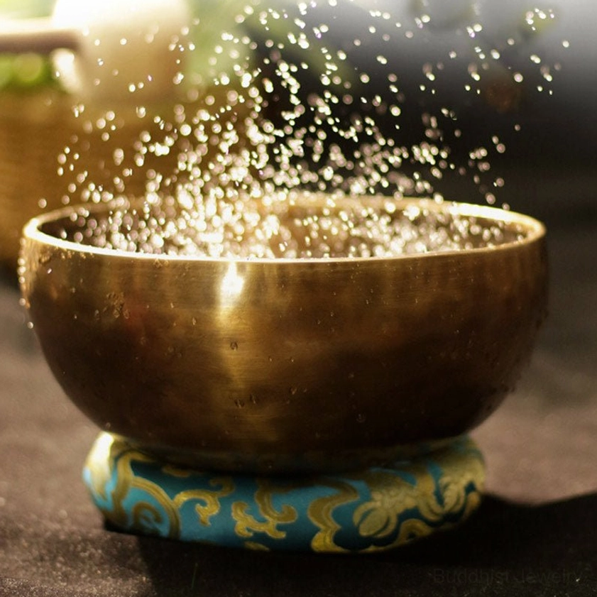 Singing bowl with water splash on blue embroidered cushion demonstrating resonance and vibration energy