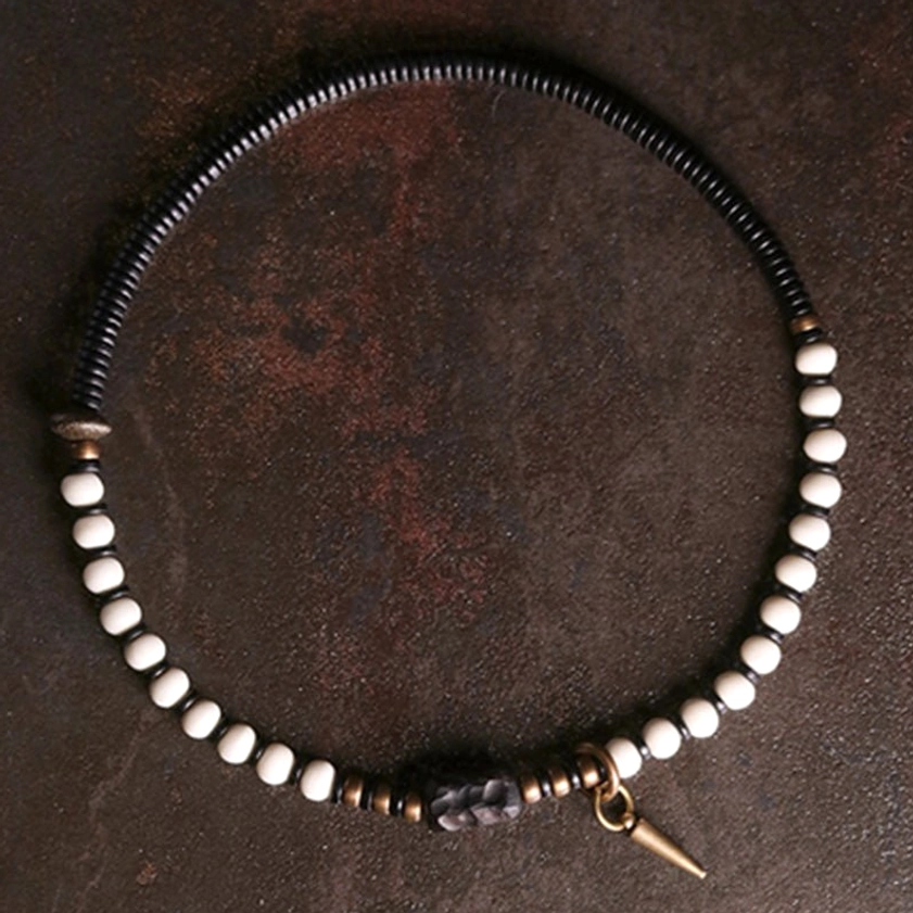 Single bone bead and ebony wood bracelet on dark leather background with bronze hardware